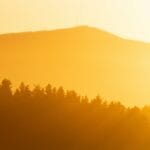the sun is setting over a mountain with trees in the foreground